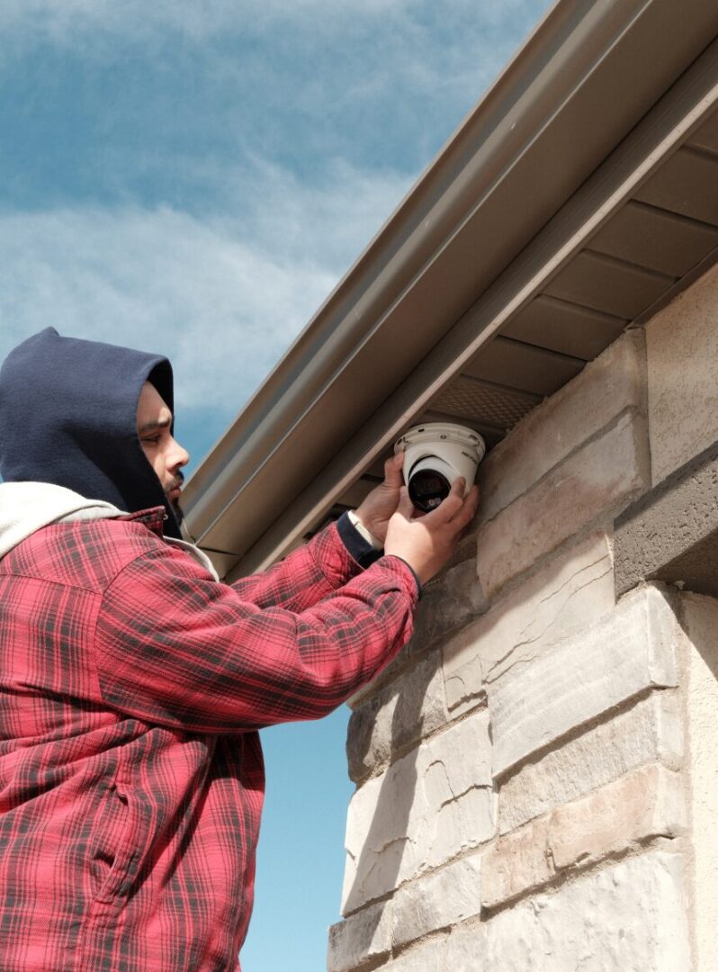 Person installing security camera under eaves.